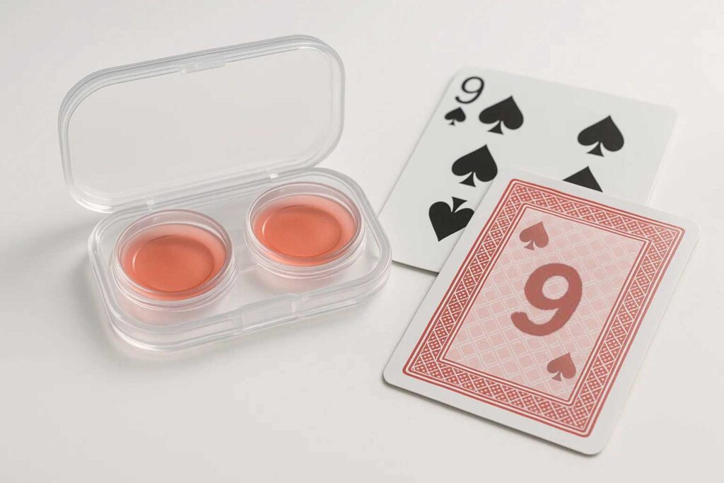 Dvojice infračervených kontaktních čoček v ochranném pouzdře vedle balíčku označených hracích karet Bicycle, které demonstrují jejich roli v Texas Hold'em pokeru.